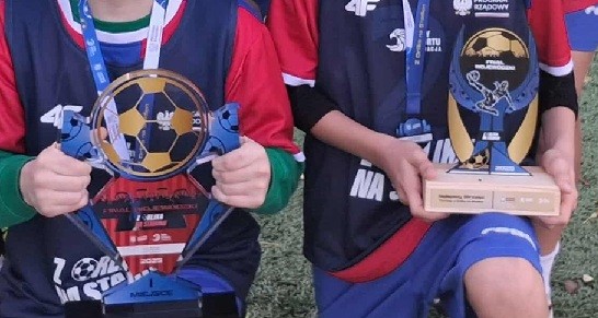 Zawodnicy trzymają trofea sportowe.