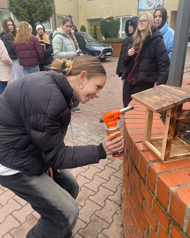 Zdjęcie przedstawia uczniów klasy 7b podczas opalania karmników.