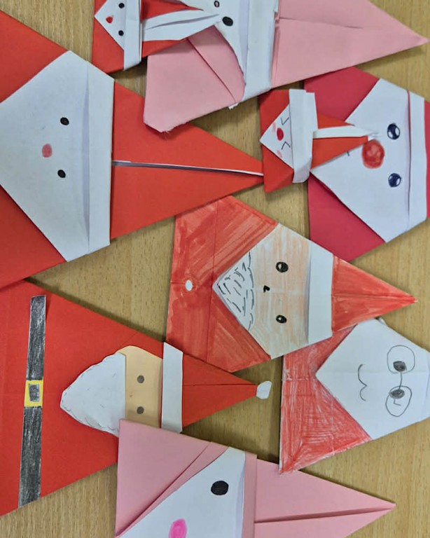 Zdjęcie przedstawia głowy mikołajów wykonane techniką origami, wykonane z czerwonego i różowego papieru.