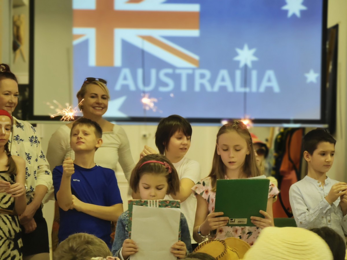 Dzień Australii w szkole. Grupa uczniów na tle flagi australijskiej omawia jak Australijczycy obchodzą swoje święto.