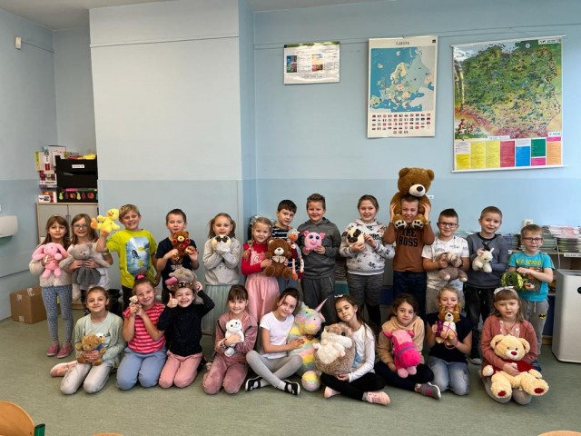 Zdjęcie przedstawia grupę uczniów wraz ze swoimi ulubionymi pluszowymi zabawkami z okazji Dnia Pluszowego Misia w szkole.