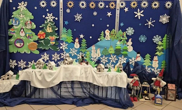 Zdjęcie przedstawia zimowy krajobraz. Niebieski pagórki na których znajdują się świąteczne choinki, bałwanki oraz małe domy wykonane z tektury.